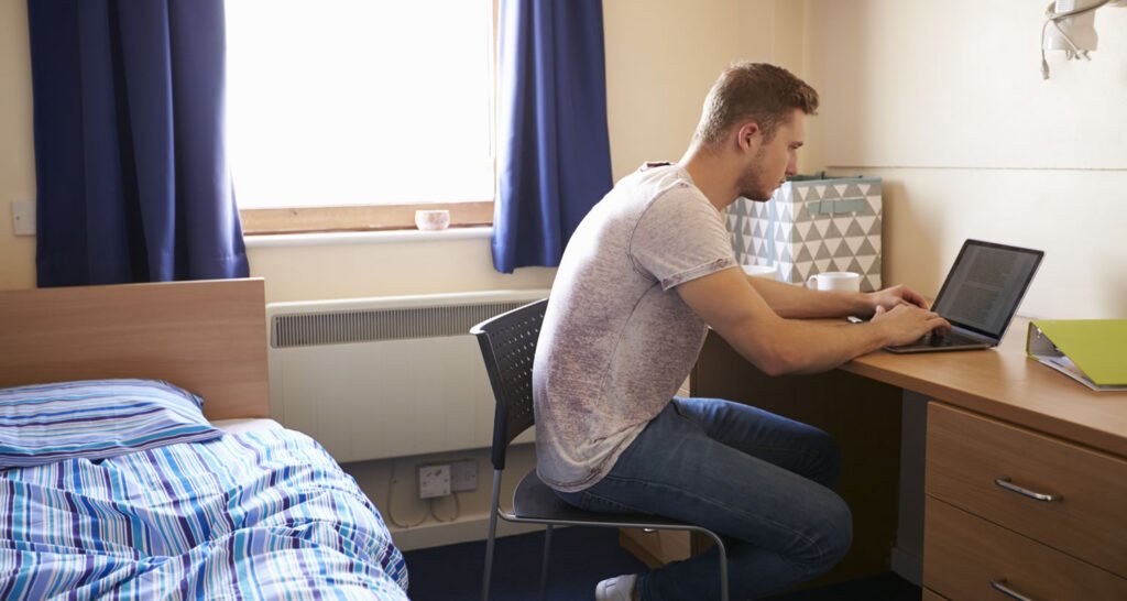 Male Student Working In Bedroom Of Campus Accommodation