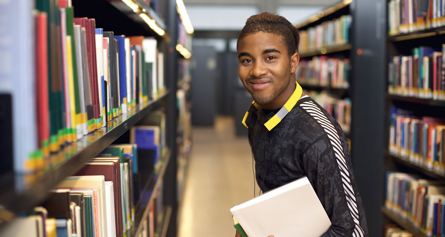 Smiling student in library holding text book