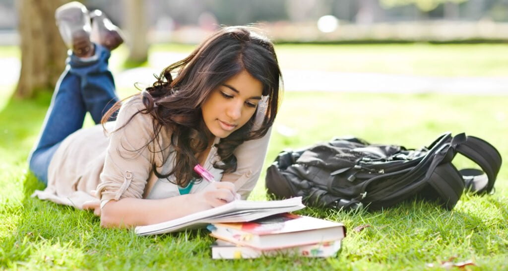 Student laying on grass writing in notebook