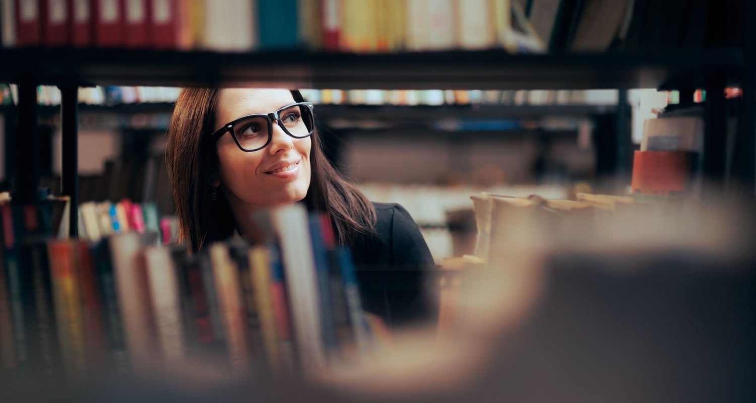 View of student looking at books seen through bookcase